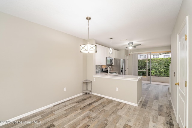 kitchen featuring a peninsula, white cabinetry, light wood-style flooring, appliances with stainless steel finishes, and backsplash