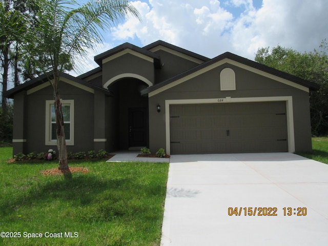 view of front of home with a garage, stucco siding, a front lawn, and driveway