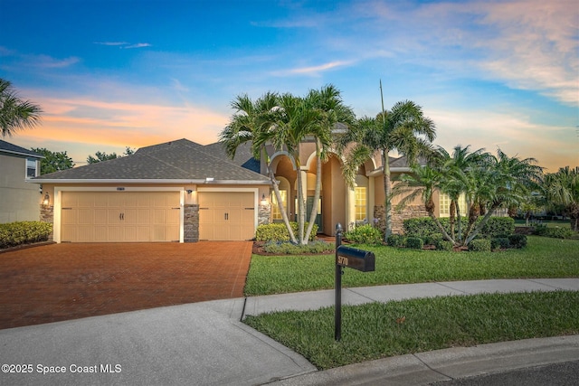 5770 Mascaro Ct, Melbourne, FL 32940 - view of front facade with driveway, stucco siding, a garage, stone siding, and a lawn