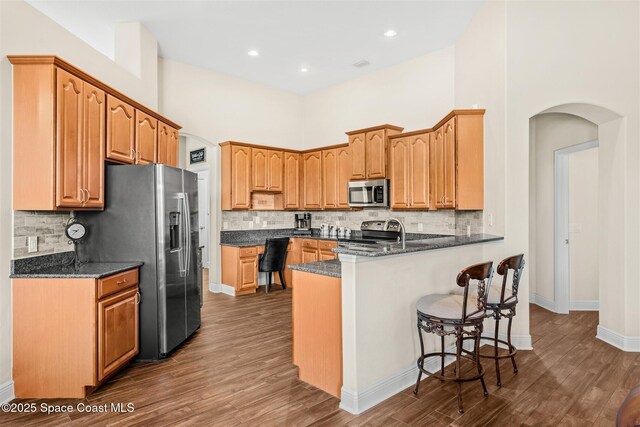 5770 Mascaro Ct, Melbourne, FL 32940 - kitchen featuring stainless steel appliances, arched walkways, a peninsula, a breakfast bar, and dark wood-type flooring