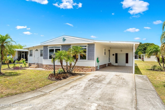 manufactured / mobile home with concrete driveway, entry steps, an attached carport, and a front lawn