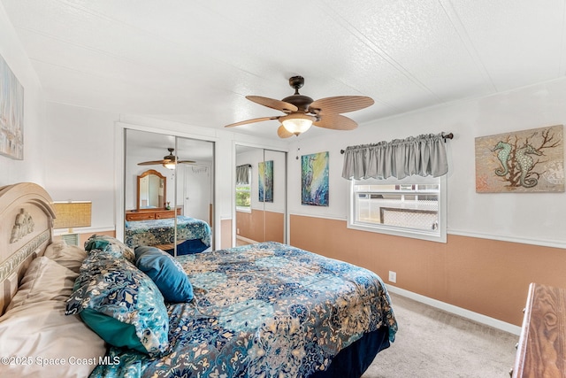 bedroom with a textured ceiling, carpet, multiple closets, a ceiling fan, and baseboards