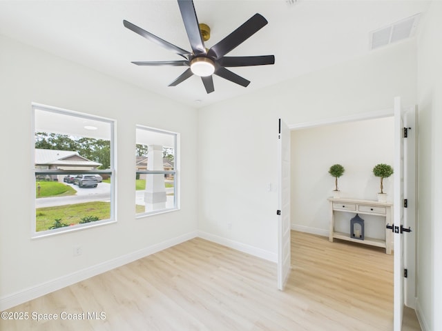 empty room with a ceiling fan, visible vents, wood finished floors, and baseboards