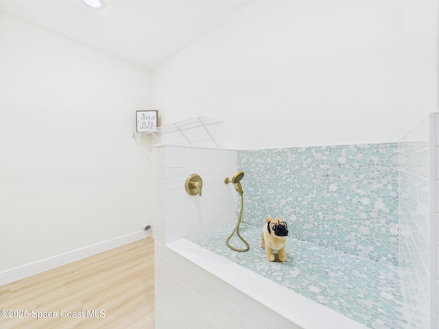 bathroom with wood finished floors, baseboards, and a tile shower