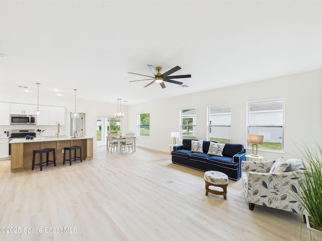 living area featuring baseboards, light wood-style floors, and ceiling fan with notable chandelier