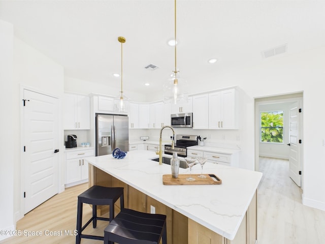 kitchen featuring stainless steel appliances, a kitchen island with sink, visible vents, white cabinetry, and light wood-style floors