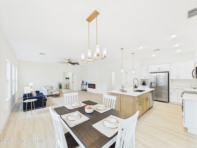 dining area with light wood finished floors, ceiling fan with notable chandelier, and visible vents