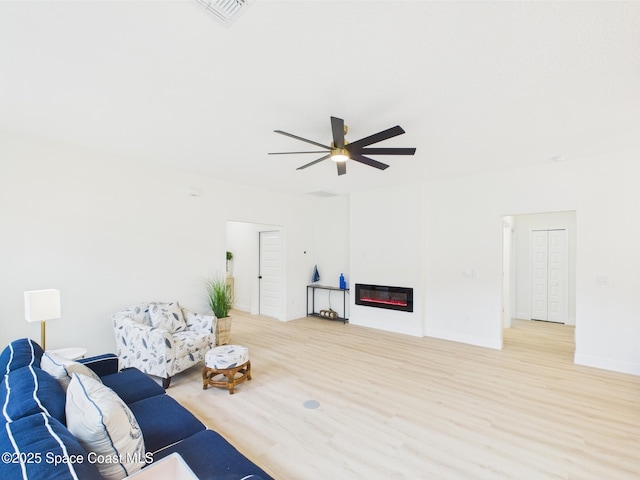 living area featuring a ceiling fan, light wood-style flooring, visible vents, and a glass covered fireplace