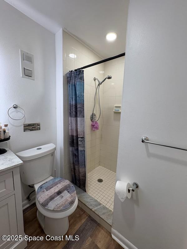 bathroom featuring toilet, visible vents, wood finished floors, and a tile shower
