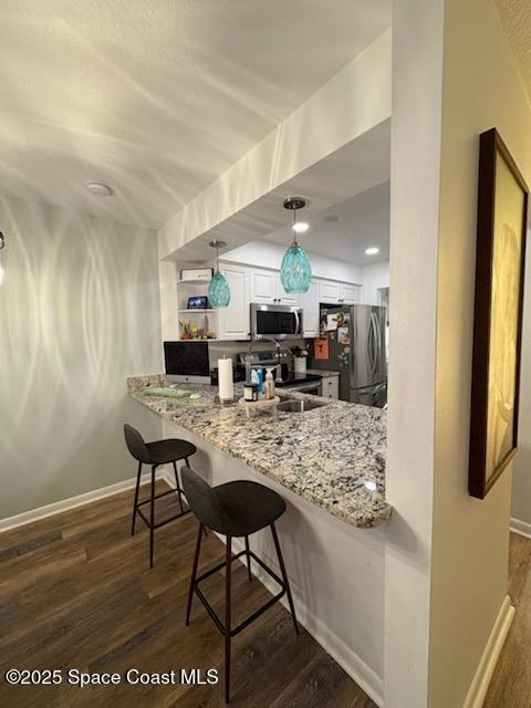 kitchen with white cabinets, light stone counters, stainless steel appliances, and dark wood-style flooring