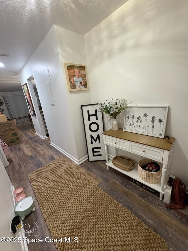 hallway featuring dark wood-style flooring, baseboards, and a textured ceiling