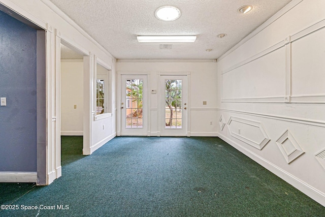 empty room featuring a textured ceiling, dark carpet, and baseboards