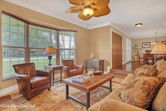 living area with ornamental molding, a wealth of natural light, baseboards, and ceiling fan with notable chandelier