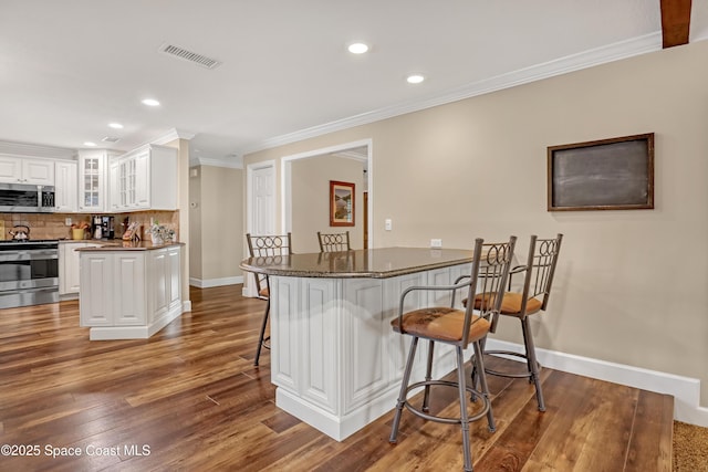 kitchen featuring baseboards, visible vents, a kitchen bar, stainless steel appliances, and white cabinets