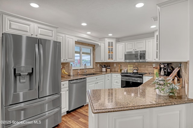 kitchen with white cabinetry, appliances with stainless steel finishes, light stone counters, and a sink