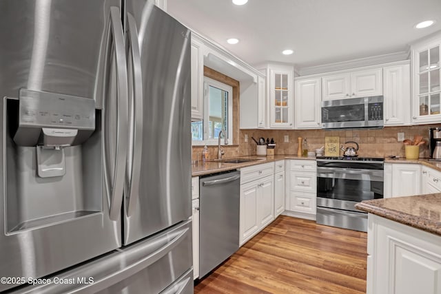 kitchen with a sink, light stone countertops, white cabinets, and appliances with stainless steel finishes