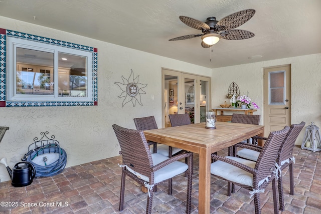 dining room featuring ceiling fan, a textured wall, french doors, and stone tile floors