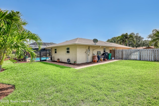 rear view of property with a lawn, a fenced in pool, fence, stucco siding, and a lanai
