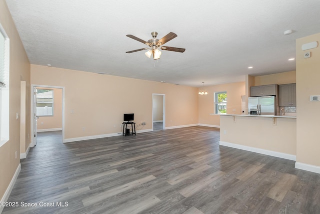 unfurnished living room with recessed lighting, ceiling fan with notable chandelier, baseboards, and dark wood finished floors