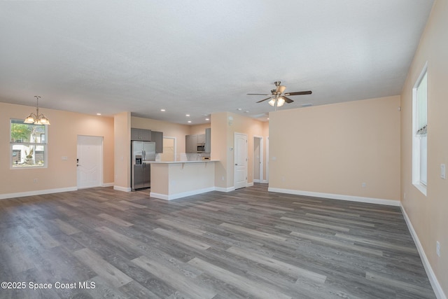 unfurnished living room featuring baseboards, dark wood-style flooring, recessed lighting, and ceiling fan with notable chandelier