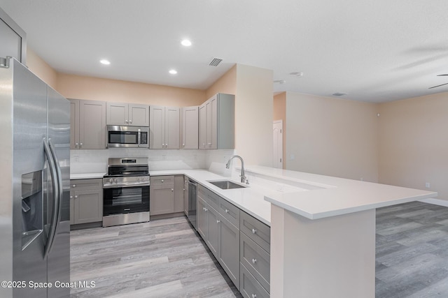 kitchen with a peninsula, light wood-style flooring, gray cabinetry, and appliances with stainless steel finishes