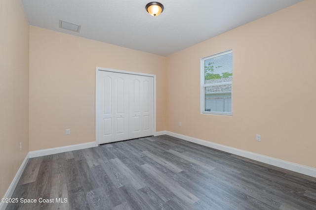 unfurnished bedroom featuring baseboards, a closet, visible vents, and dark wood-type flooring