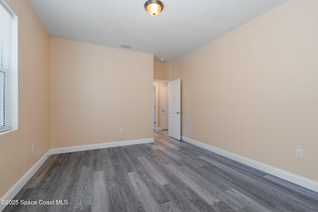 empty room featuring a wealth of natural light, dark wood finished floors, visible vents, and baseboards