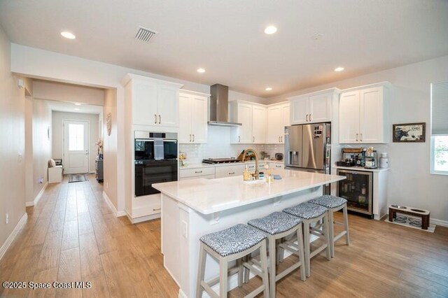 2979 Pangea Cir, Melbourne, FL 32940 - kitchen with wall chimney range hood, stainless steel fridge with ice dispenser, beverage cooler, multiple ovens, and light wood-style floors