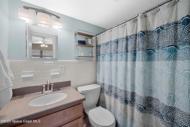 bathroom featuring toilet, a ceiling fan, a wainscoted wall, tile walls, and vanity