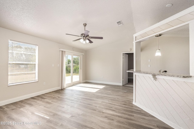 unfurnished living room with a ceiling fan, light wood-type flooring, baseboards, vaulted ceiling, and a textured ceiling