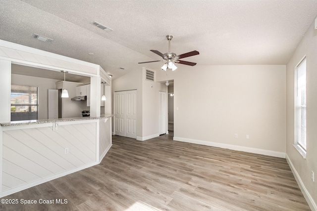 unfurnished living room featuring a textured ceiling, plenty of natural light, vaulted ceiling, ceiling fan, and wood finished floors