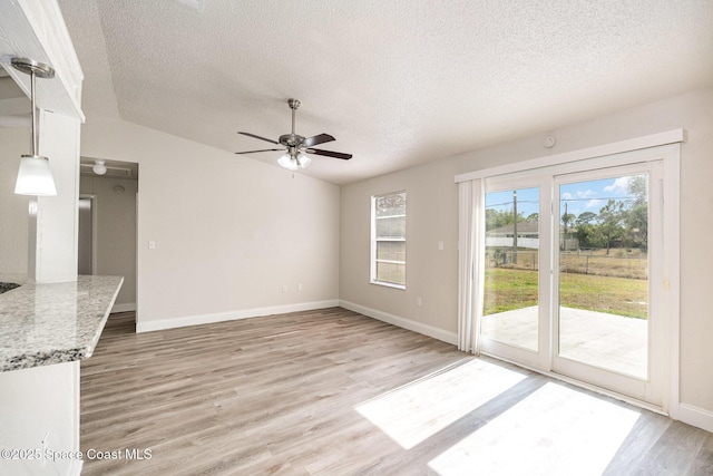 unfurnished living room featuring a textured ceiling, light wood finished floors, a ceiling fan, baseboards, and vaulted ceiling