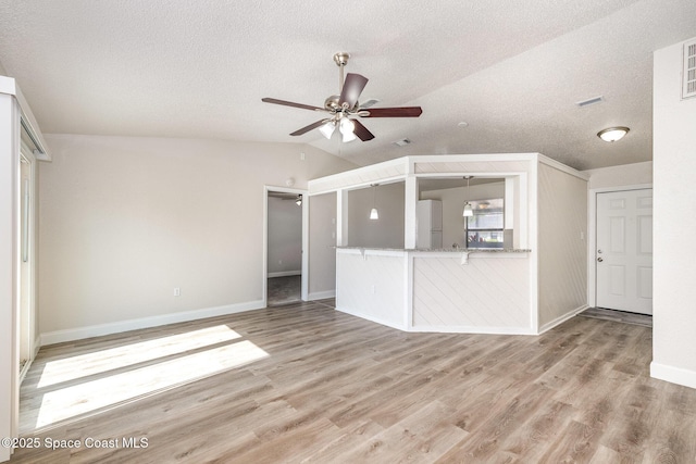 unfurnished living room with vaulted ceiling, a ceiling fan, baseboards, wood finished floors, and a textured ceiling