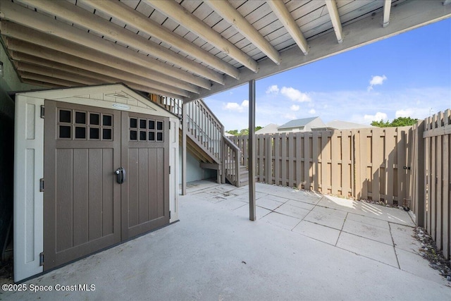 view of patio featuring stairs, an outdoor structure, fence, and a storage unit