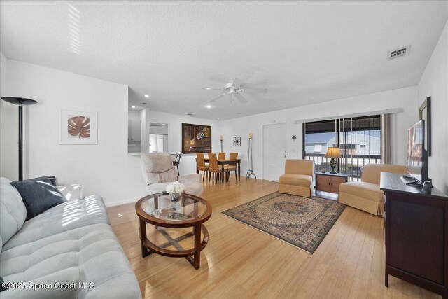 living room featuring a ceiling fan, light wood-type flooring, visible vents, baseboards, and recessed lighting