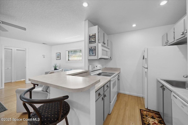 kitchen featuring white appliances, ceiling fan, a sink, light countertops, and light wood-type flooring
