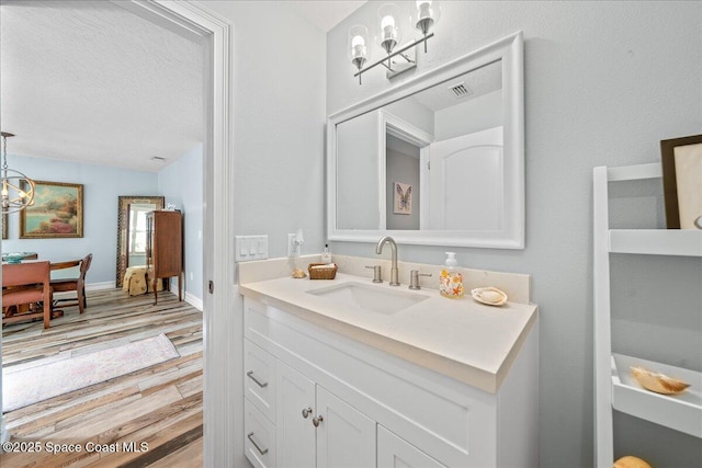 505 Tradewinds Dr, Indian Harbour Beach, FL 32937 - bathroom with a textured ceiling, an inviting chandelier, visible vents, vanity, and wood finished floors