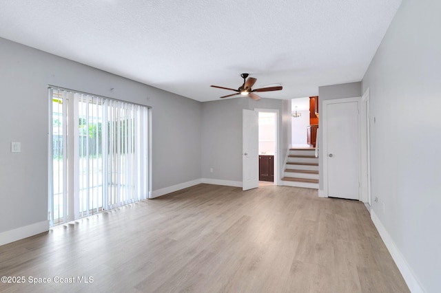 unfurnished living room with light wood-style floors, ceiling fan, baseboards, stairs, and a textured ceiling