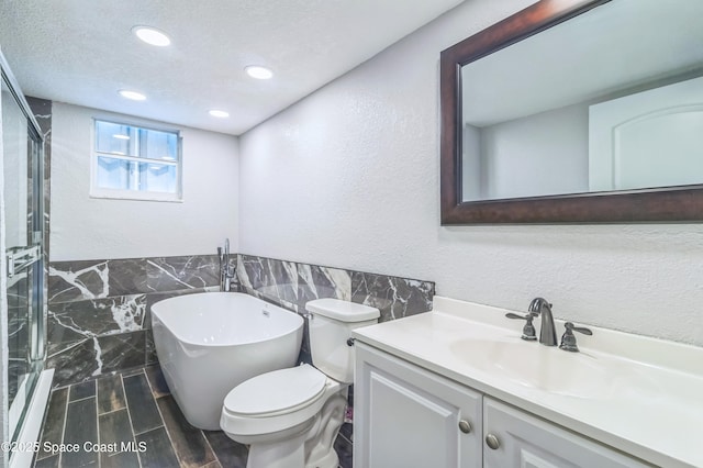 full bathroom with tile walls, a textured wall, a stall shower, vanity, and a freestanding tub