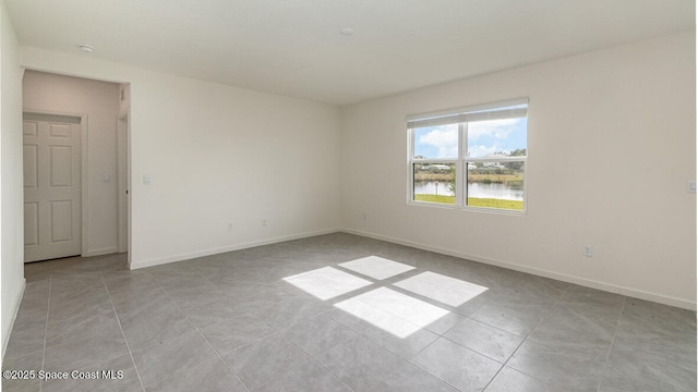 unfurnished room with light tile patterned floors, baseboards, and a water view
