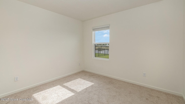 spare room featuring light carpet and baseboards