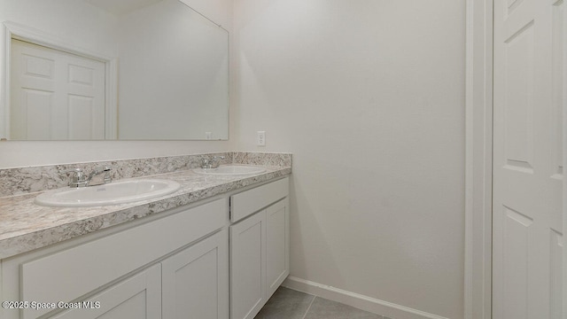 bathroom with baseboards, tile patterned floors, double vanity, and a sink