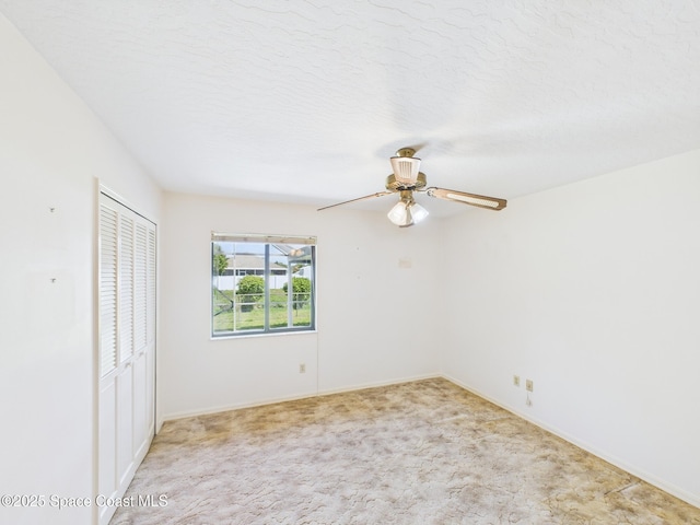spare room with light colored carpet, a textured ceiling, baseboards, and ceiling fan