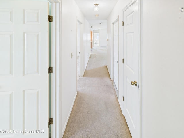 hallway featuring light colored carpet and baseboards
