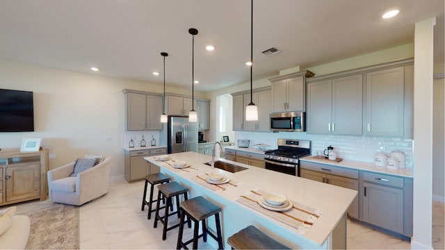 kitchen featuring a sink, stainless steel appliances, gray cabinets, marble finish floor, and a kitchen bar