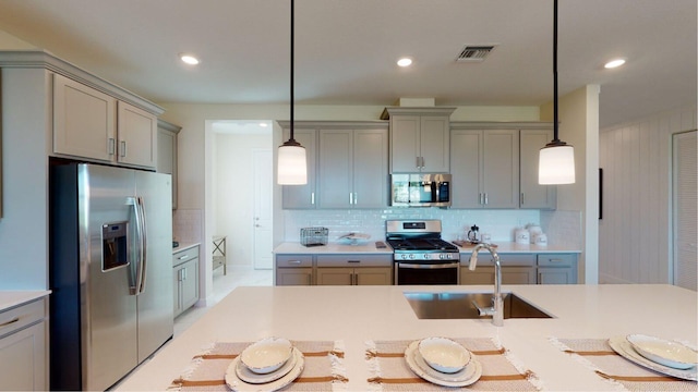 kitchen with a sink, gray cabinets, light countertops, appliances with stainless steel finishes, and tasteful backsplash