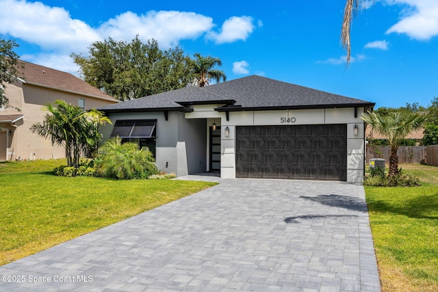 prairie-style house with an attached garage, stucco siding, a shingled roof, decorative driveway, and a front yard