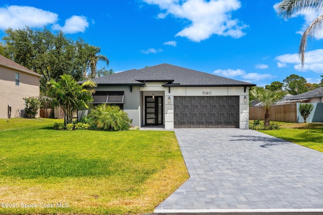 prairie-style home featuring fence, an attached garage, stucco siding, a front yard, and decorative driveway