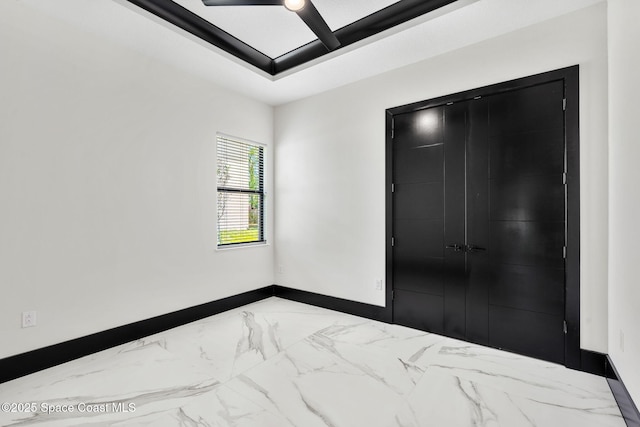 unfurnished bedroom featuring baseboards, a ceiling fan, marble finish floor, and a closet
