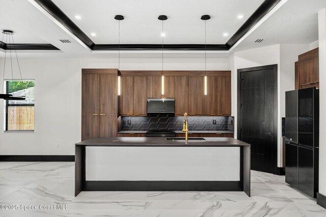 kitchen featuring a sink, brown cabinetry, tasteful backsplash, a tray ceiling, and dark countertops